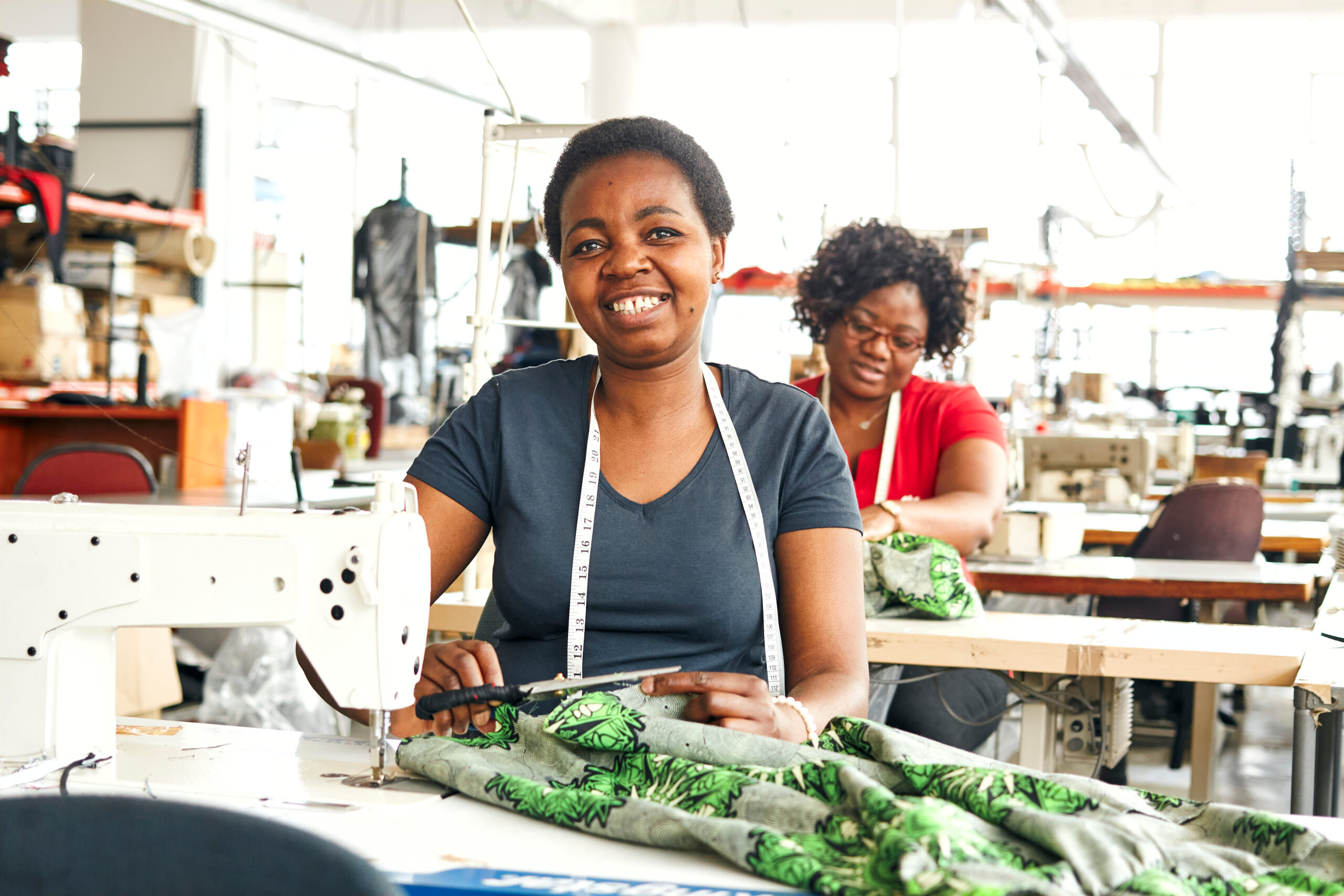 Two,Black,African,Zimbabwean,Ladies,Working,In,A,Textile,Factory Eine dunkelhäutige Frau sitzt vor einer Nähmaschine in einer Textilfabrik